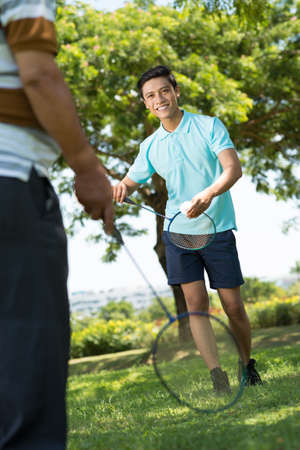 Vertical image of a young grandson playing badminton with his grandfather on the foregroundの写真素材