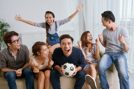 Young friends cheering for soccer team at homeの写真素材