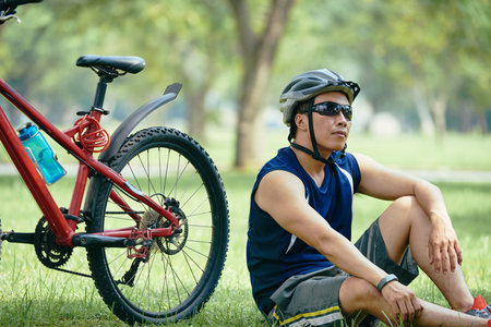 Cyclist resting on grass in park after rideの写真素材