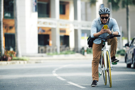 Smiling Asian man text messaging when cycling along the road