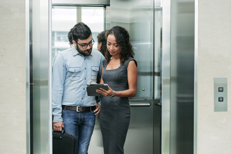 Business people standing in elevator and discussing data on tablet computer