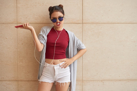 Angry young woman in sunglasses standing at the wallの写真素材
