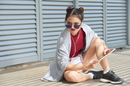 Unhappy Vietnamese teenage girl sitting on ground with tablet computerの写真素材