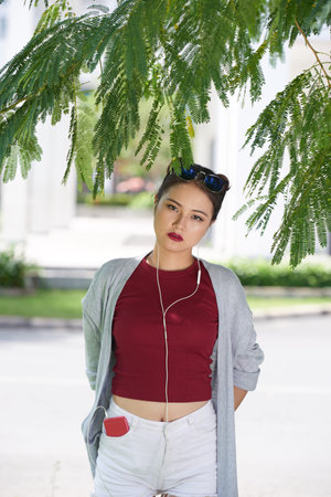 Portrait of Vietnamese young woman standing under the tree and looking at camera