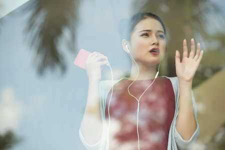 Surprised young woman looking through the windowの写真素材