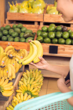 Woman choosing ripe bananas at organic marketの写真素材