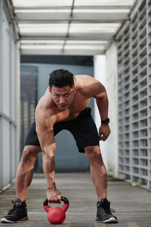 Sportsman looking at camera when lifting kettlebellの写真素材