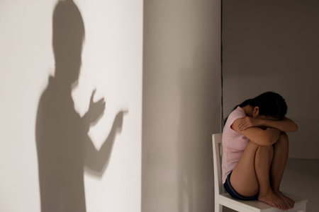 Image of a depressed teenage girl sitting on the chair while her father?s silhouette quarreling on the foregroundの写真素材