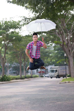 Boy sitting in the air with an umbrellaの写真素材