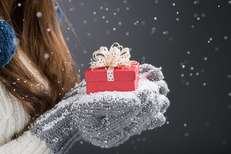 Close-up of a red giftbox in female hands in knitted mittens