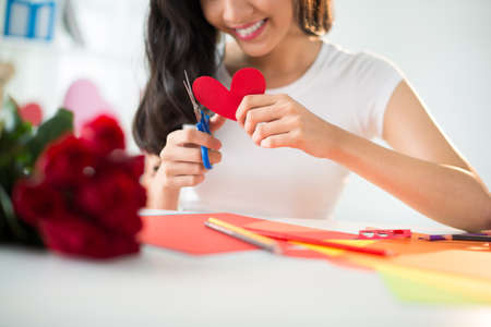Close-up of female hands scissoring out paper heartの写真素材