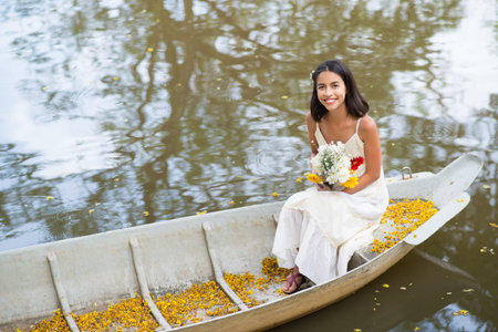 Copy-spaced portrait of a summer girl with flower bunches sitting in the boat and looking at cameraの写真素材