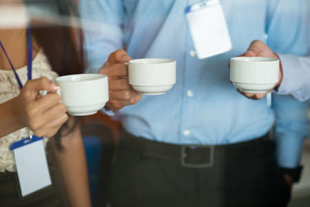 Close-up of tea cups in hands of office workersの写真素材