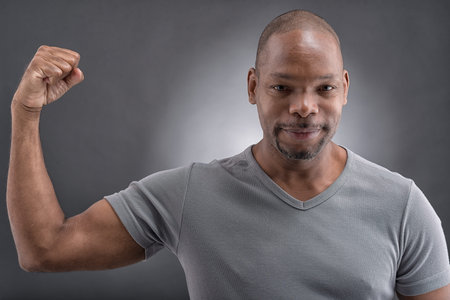 Close-up portrait of a strong young guy showing his muscular over a grey background