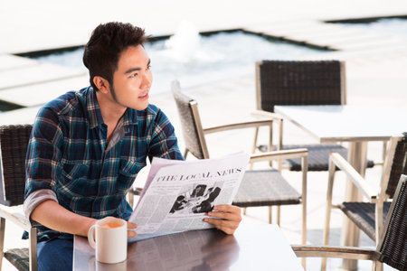 Angle view of a young man reading the newspaper at cafeの写真素材