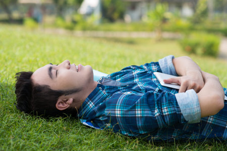 Closeup image of a student with a tablet lying on the grass in the campusの写真素材