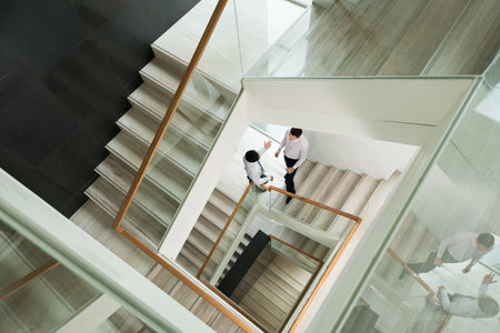Two white-collars discussing something standing on the staircase