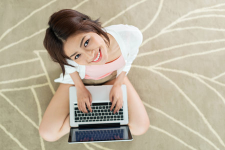 Vietnamese young lady using notebook while sitting on the floor, view from above
