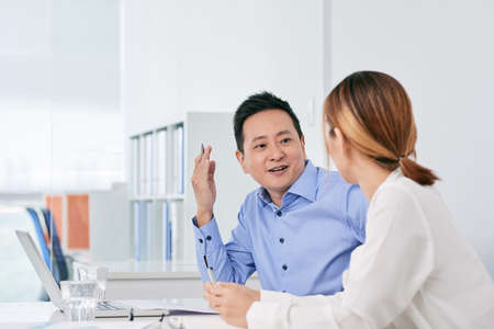 Cheerful Asian businessman talking to female coworker in officeの写真素材
