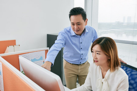 Asian businessman showing information on computer screen to coworker