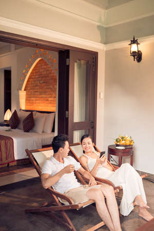 Vertical image of a young couple sitting in chaise lounges in resort hotel on the foregroundの写真素材