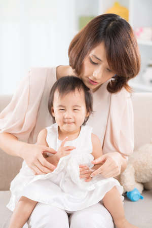 Chinese girl sitting on mom?s knees at homeの写真素材