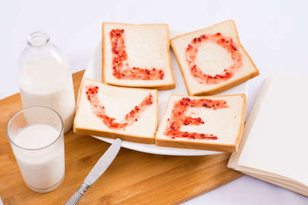 Close-up of a morning breakfast where a glass of fresh milk and toasts with jam with the symbol of loveの写真素材