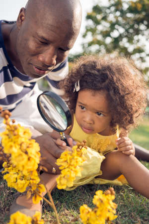 Closeup image of a father looking at the yellow flowers through the magnifier with his little daughter on the foregroundの写真素材