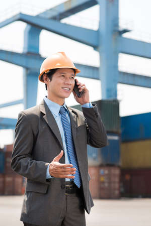 Vertical image of a smiley port worker talking by phone in industry areaの写真素材