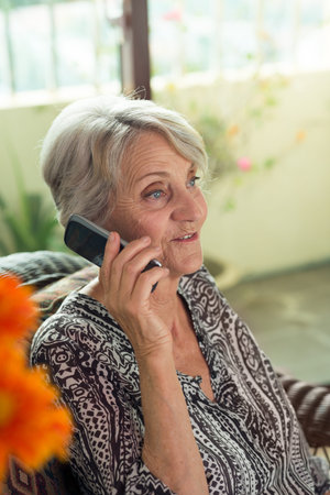 Old woman sitting in an armchair talking on her phone