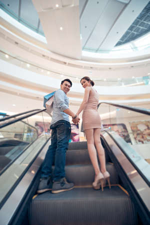 Happy couple standing on the escalator in the mall, view from belowの写真素材