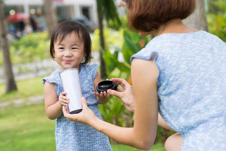 Chinese woman giving her daughter a glass of milk outdoorsの写真素材