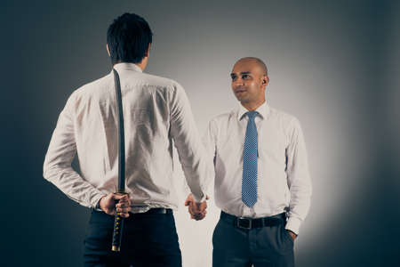 Businessman shaking hands with his partner while hiding katana sword behind his backの写真素材