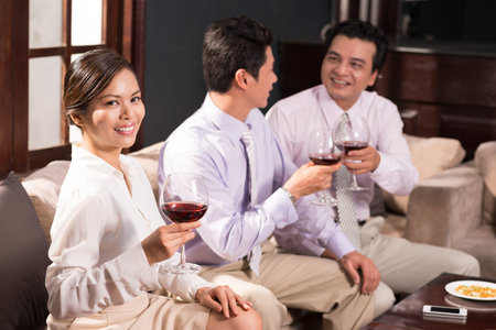 Portrait of pretty businesswoman holding a glass of wine while spending time with her coworkers in...