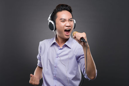 Portrait of young Asian man wearing headphones and singing into microphoneの写真素材