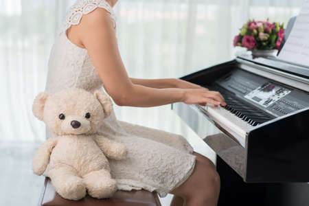 Unrecognizable girl playing piano when her teddy bear is sitting by herの写真素材