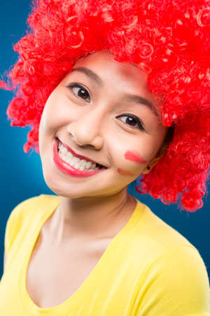 Close-up of joyful Asian girl wearing red curly wigの写真素材