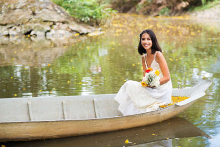 Happy young lady with a bouquet sitting in the boatの写真素材