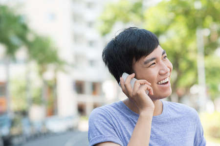 Portrait of young joyful man talking on the phone outdoorsの写真素材