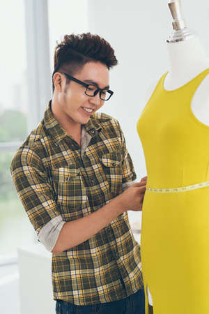 Vietnamese dressmaker measuring a mannequin in yellow dressの写真素材