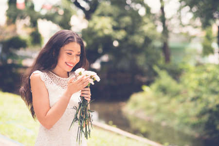 Beautiful young woman smelling flowers in the parkの写真素材