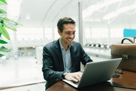 Happy manager working on his laptop in the waiting room of the airportの写真素材