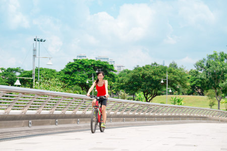 Joyful girl riding on bike across the bridgeの写真素材