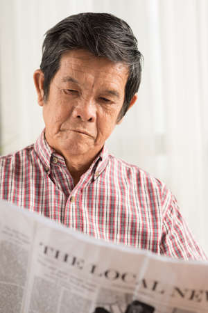 Serious Asian man reading newspaperの写真素材