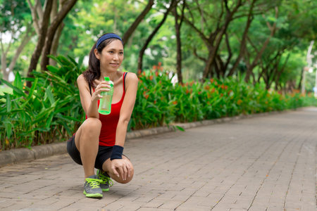Female runner resting and drinking cold water in the parkの写真素材