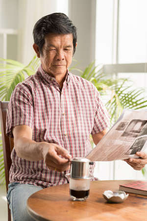 Senior Asian man drinking coffee and reading morning newspaperの写真素材