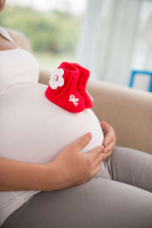 Close-up of red knitted baby shoes on the belly of pregnant womanの写真素材
