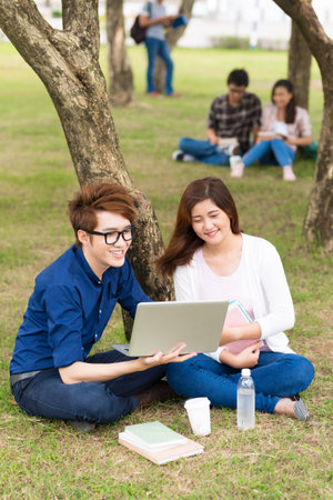Young couple watching something on the laptop while resting on campus