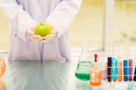 Cropped image of scientist with green apple standing near table with laboratory glasswareの写真素材