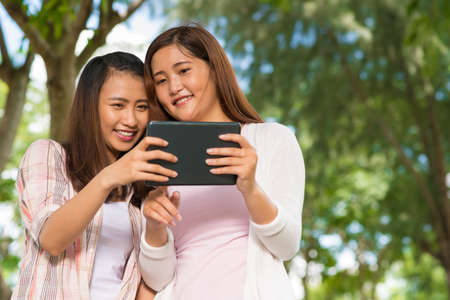 Two Vietnamese teenage girls using digital tablet outdoorsの写真素材